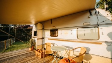 Travel trailer toy hauler with open ramp patio, showing an ATV and people enjoying a scenic outdoor adventure, highlighting versatile RV living.