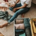 Woman packing a travel size face wash and other essential skincare items into a carry-on bag for a trip, ensuring a consistent and healthy skin routine while traveling.