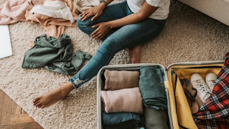 Woman packing a travel size face wash and other essential skincare items into a carry-on bag for a trip, ensuring a consistent and healthy skin routine while traveling.