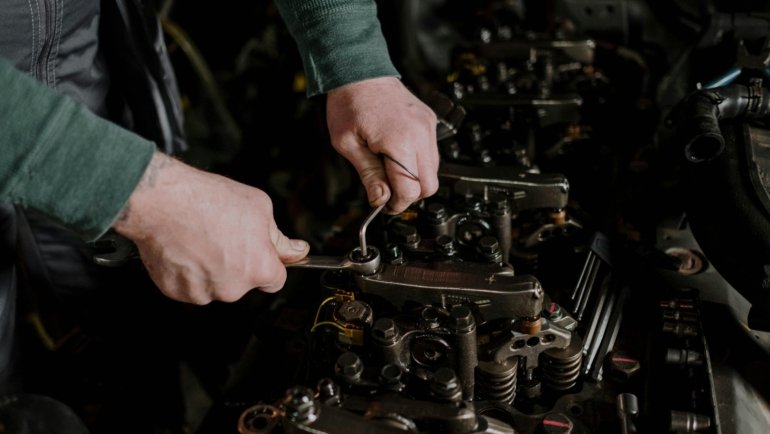 Close-up of hands performing Concept 2 rowing machine travelling pulley assembly maintenance, cleaning dust and inspecting for smooth chain movement.