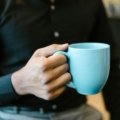 Stylish double-walled ceramic travel mug with lid, filled with hot coffee or tea, held for a pure taste experience on a daily commute.