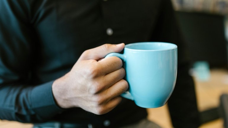 Stylish double-walled ceramic travel mug with lid, filled with hot coffee or tea, held for a pure taste experience on a daily commute.
