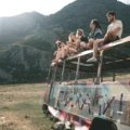 Diverse young backpackers with backpacks smiling on a hop-on hop-off 'traveller bus' against a beautiful natural backdrop, symbolizing budget-friendly, social, and adventurous travel exploration.