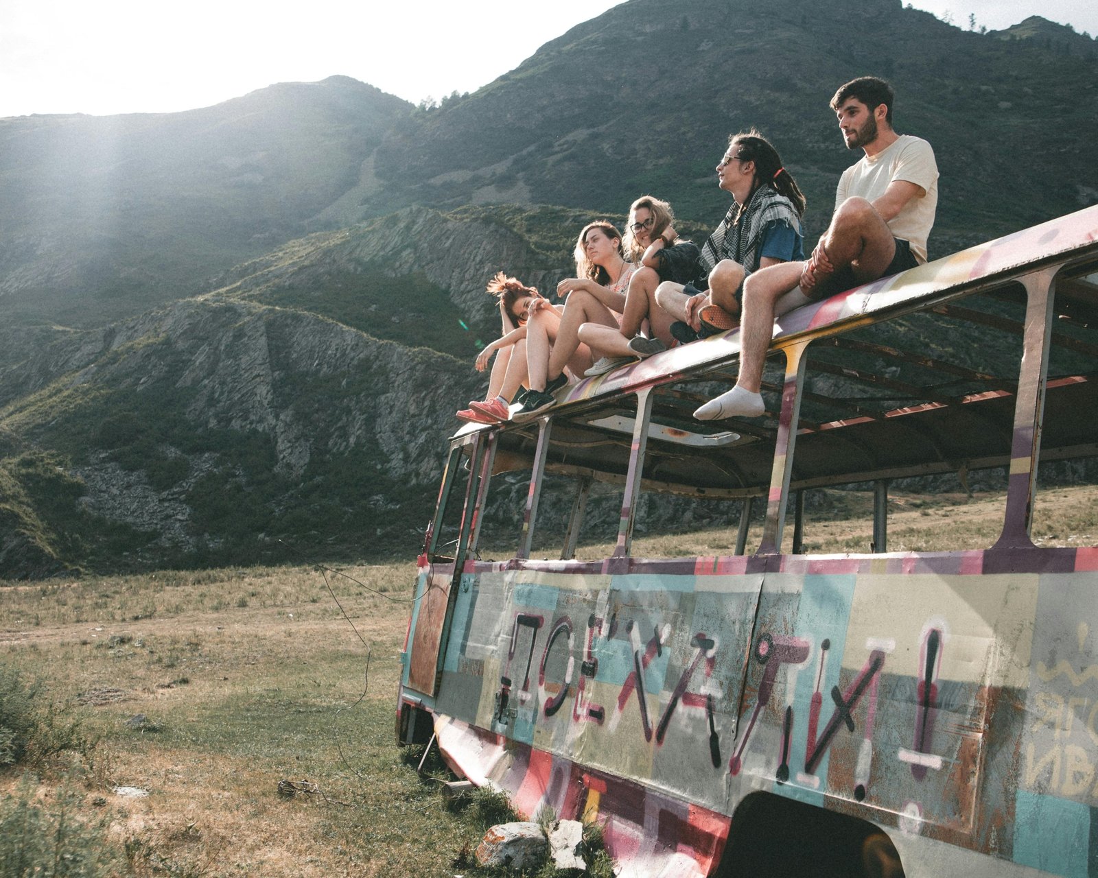 Diverse young backpackers with backpacks smiling on a hop-on hop-off 'traveller bus' against a beautiful natural backdrop, symbolizing budget-friendly, social, and adventurous travel exploration.