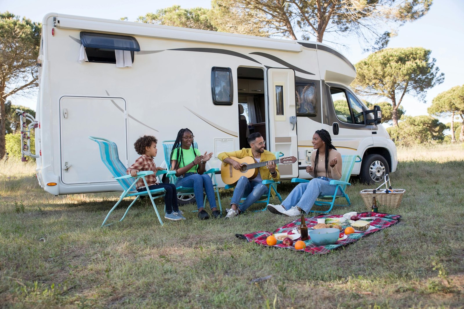 A modern travel trailer with a gray slide-out awning (slide topper) extended, providing essential protection from sun, rain, and debris for the RV's slide-out in a scenic outdoor camping environment.