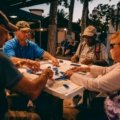 Happy friends playing with a portable travel mahjong set on a sunny outdoor vacation, highlighting its compact design and social enjoyment.