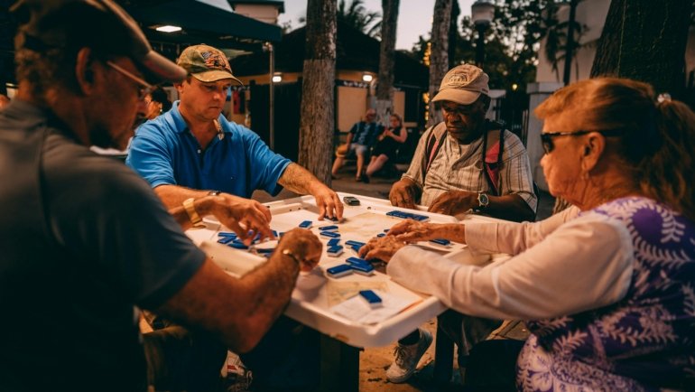 Happy friends playing with a portable travel mahjong set on a sunny outdoor vacation, highlighting its compact design and social enjoyment.