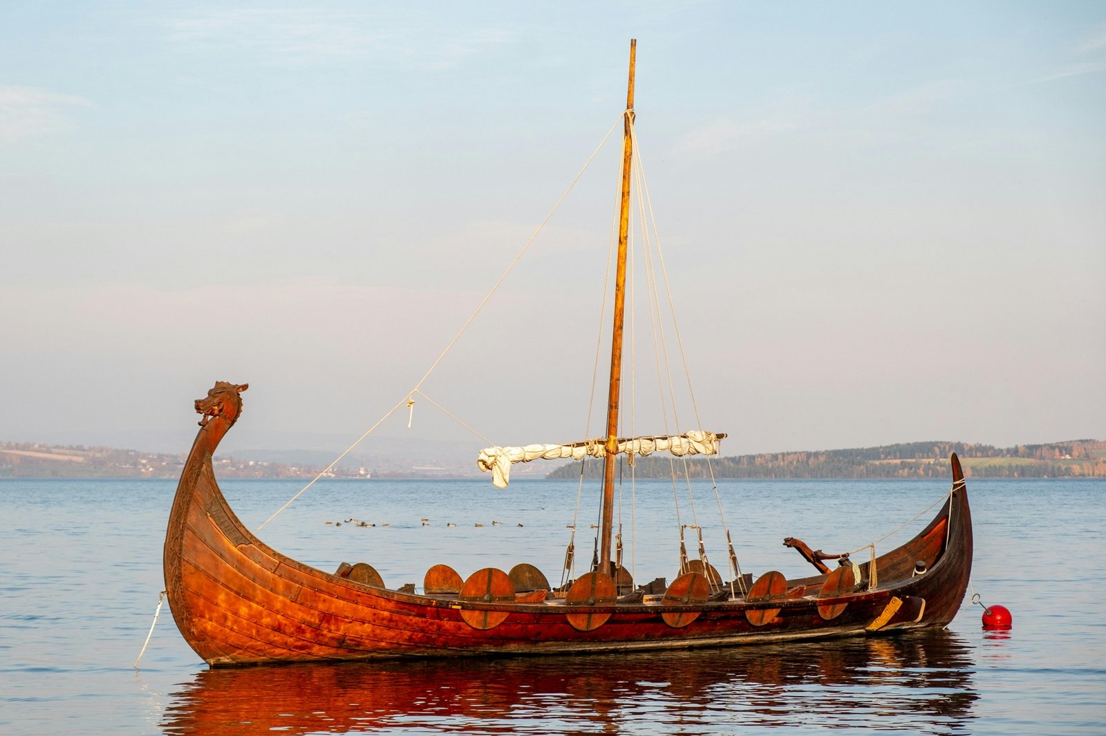 Majestic Viking longship with a prominent dragon head carving and large square sail, navigating open waters, symbolizing ancient Norse naval engineering, exploration, and trade.