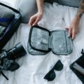 Traveler packing elegant travel-sized perfumes and solid fragrances into a clear carry-on bag, demonstrating smart techniques for airport security and spill prevention.