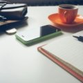 A hands-on view of an open leather Midori Traveler's Notebook with a pen, ready for personalized journaling and adventure planning, surrounded by travel maps and a hot beverage.