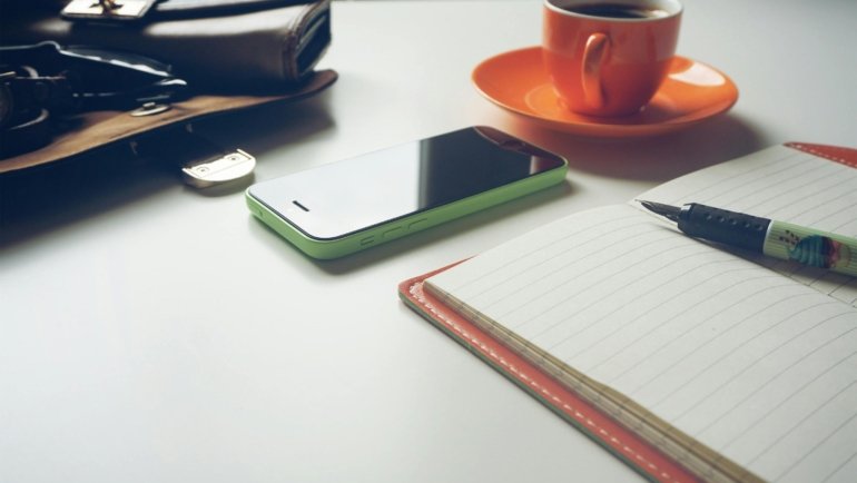 A hands-on view of an open leather Midori Traveler's Notebook with a pen, ready for personalized journaling and adventure planning, surrounded by travel maps and a hot beverage.