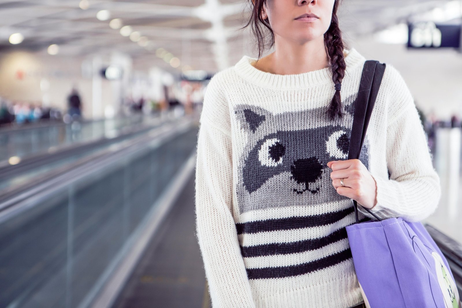 Stylish woman effortlessly walking through a modern airport terminal with a sleek travel tote bag secured to her rolling luggage handle via a trolley sleeve, illustrating hands-free and organized travel convenience.