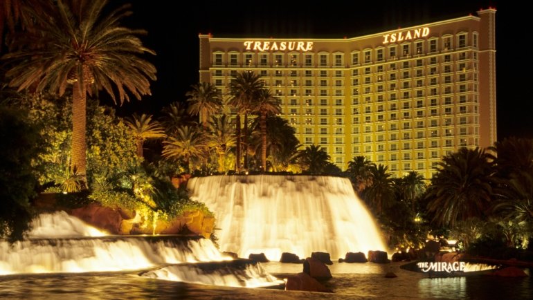 A vibrant Moapa Travel Plaza illuminated at night, contrasting with the vast Nevada desert, featuring gas pumps, a convenience store, and car activity, symbolizing a full-service oasis and key stop for I-15 road trippers supporting the Moapa Band of Paiutes.