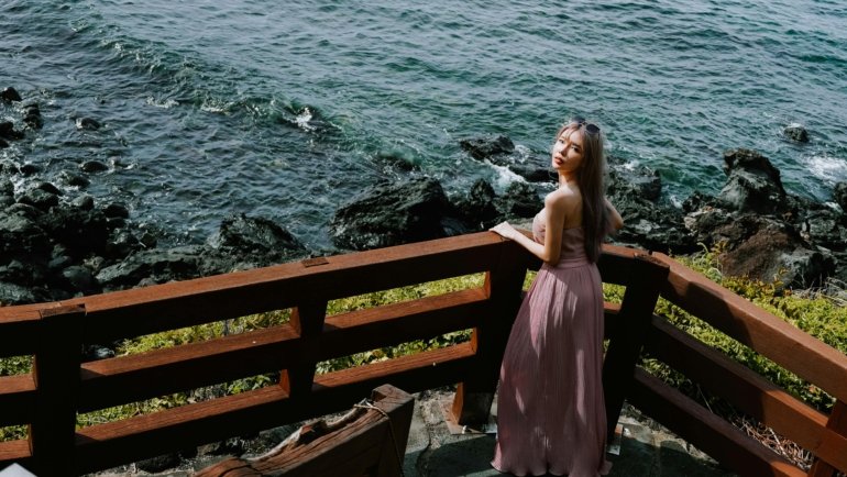 A stylish woman wearing a light pink off-the-shoulder dress while traveling, embodying comfort, versatility, and elegance for a perfect vacation wardrobe.