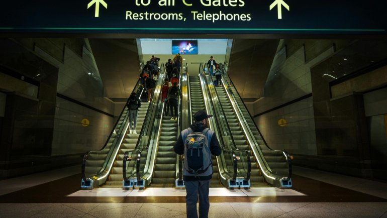 A person confidently carrying the tomtoc travel backpack 40l, a sleek and durable carry-on bag, through a bright, modern airport terminal, symbolizing efficient and organized travel.