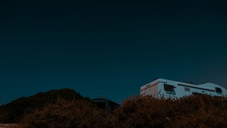 A modern travel trailer and a large fifth wheel RV parked outdoors at a scenic campsite, representing the choice between these two popular recreational vehicles for adventure and road trips.