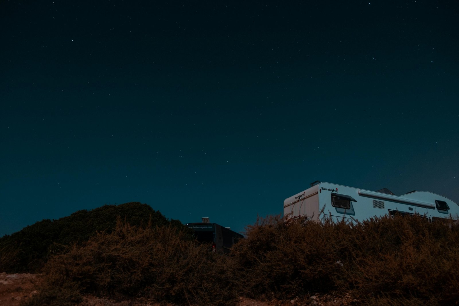 A modern travel trailer and a large fifth wheel RV parked outdoors at a scenic campsite, representing the choice between these two popular recreational vehicles for adventure and road trips.