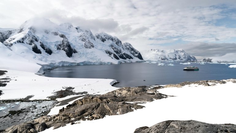 Stunning view of an expedition cruise ship sailing past colossal icebergs in the vast, icy waters of Antarctica, symbolizing the dream of polar travel and its associated costs.
