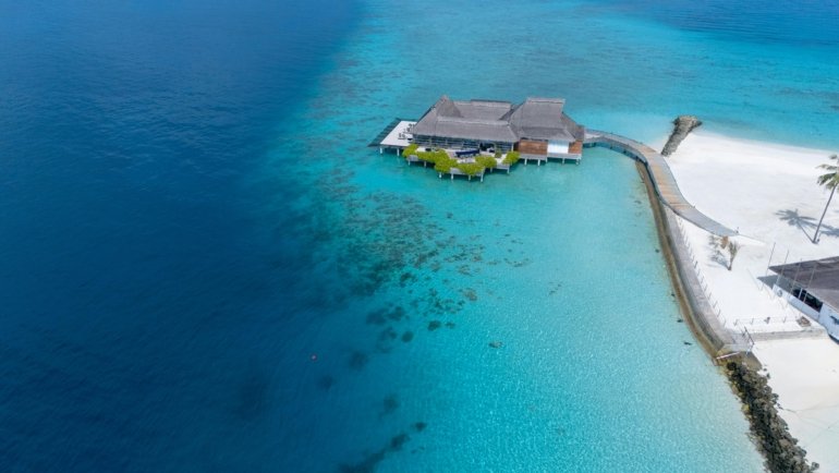 Luxury travel blog holiday inspiration: Stunning turquoise waters and white sandy beach featuring a luxurious overwater bungalow resort, epitomizing a serene tropical paradise getaway.