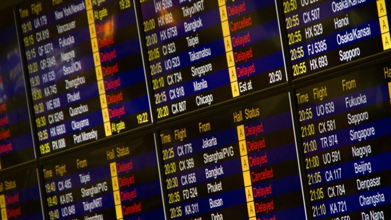 Frustrated passengers at a European airport departure terminal, looking at a board filled with cancelled and delayed flights due to a Belgium air traffic control strike, highlighting travel disruption.