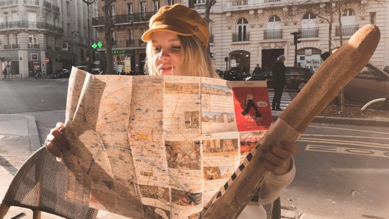 A smiling traveler planning their Paris adventure with a classic paper travel map at a charming Parisian cafe, symbolizing confident navigation and discovery in the City of Light.