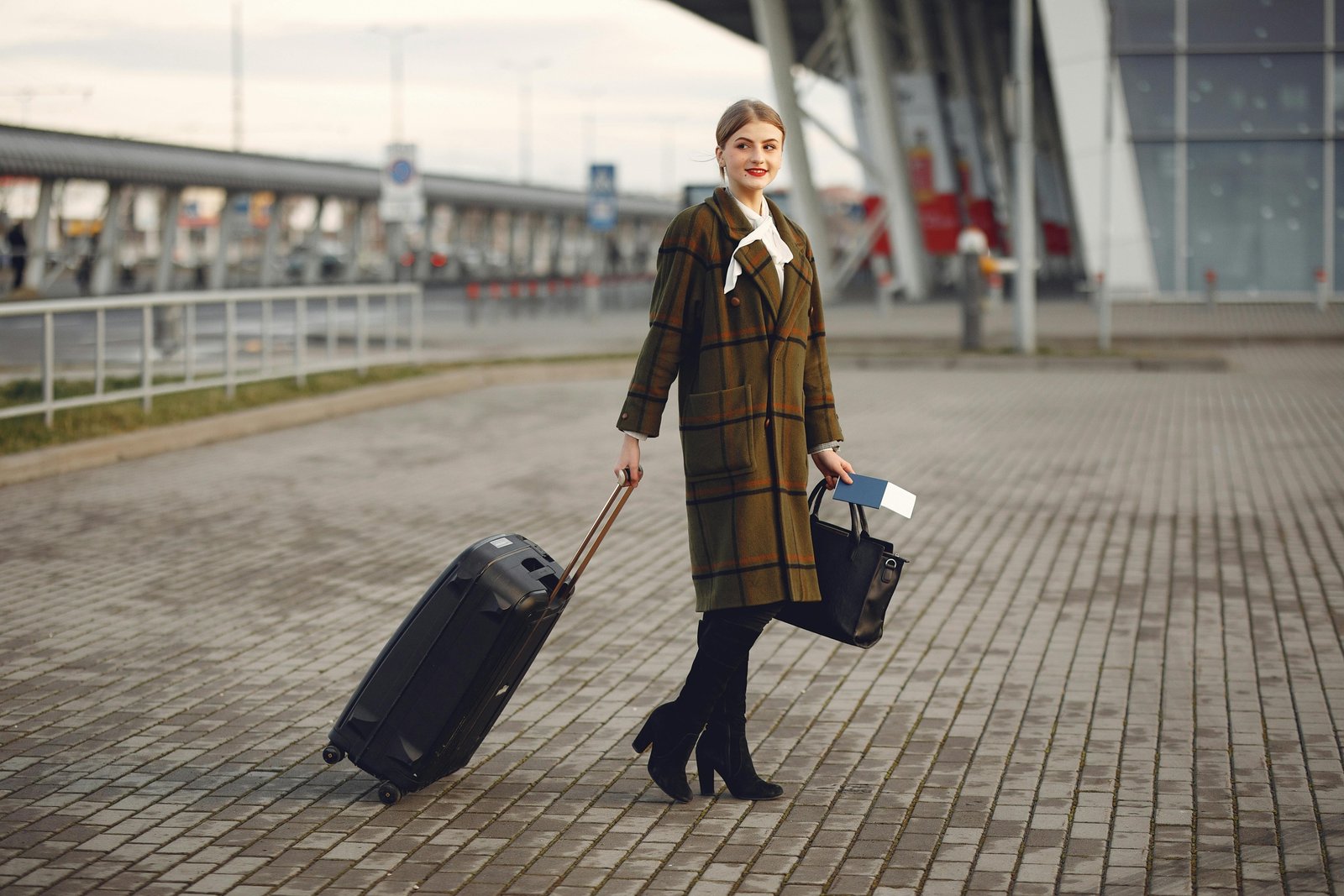 Stylish woman in an airport terminal with a modern travel tote bag on a rolling suitcase, emphasizing smart organization and travel convenience.