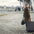 A stylish traveler confidently pulling a Guess travel suitcase through a bustling airport, emphasizing its chic design, premium features, and durability for modern journeys.