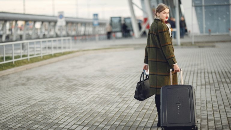 A stylish traveler confidently pulling a Guess travel suitcase through a bustling airport, emphasizing its chic design, premium features, and durability for modern journeys.