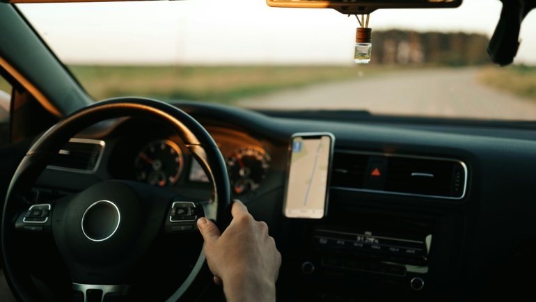 A car's dashboard with a speedometer, a road map, and a smartphone displaying a travel route, symbolizing efficient road trip planning by calculating speed, distance, and time.
