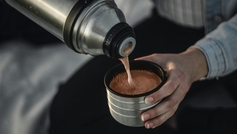 Insulated hot tea travel mug with visible steam, held by a person on the go, perfect for morning commutes, outdoor adventures, and keeping tea hot.