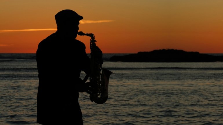 Musician happily playing a portable travel saxophone in a beautiful outdoor landscape, emphasizing freedom and convenient music practice while traveling.