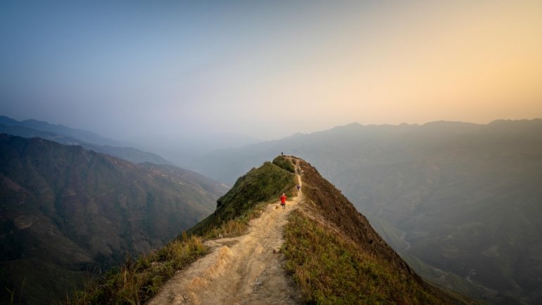 Lone traveler walking on a winding path through a vast, beautiful mountain landscape, symbolizing an inspiring journey of discovery, adventure, and personal growth, ideal for wanderlust and travel quotes.