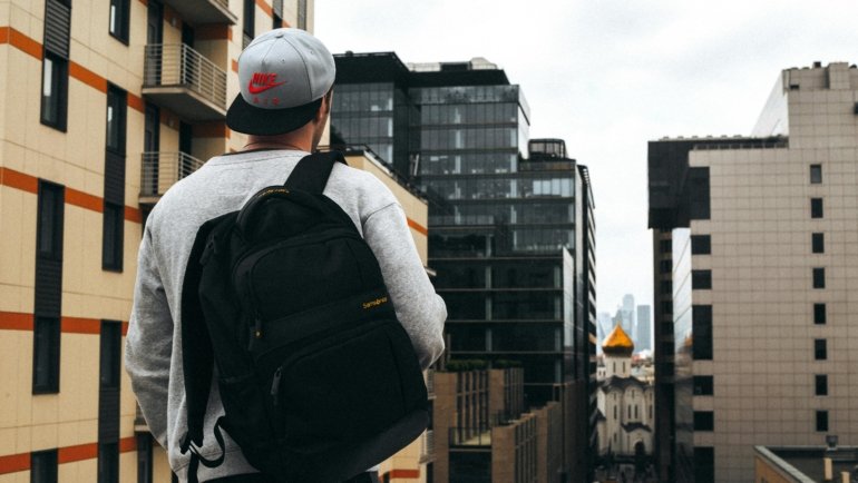 A modern traveler, casually walking with a versatile carry-on travel pack (similar to Osprey Porter 46) through a city street or airport, embodying efficient one-bag travel for digital nomads and weekend adventurers.