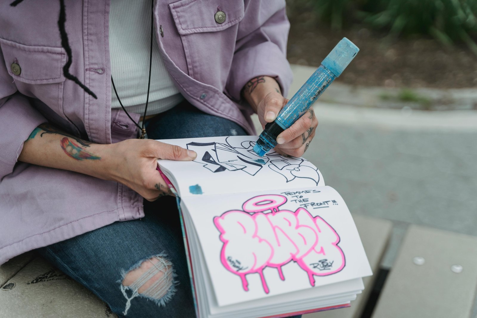 Close-up of hands sketching in a travel journal or sketchbook with a fineliner pen, overlooking a scenic European city street or a cozy cafe, illustrating the mindful art of travel drawing and creating personal souvenirs.