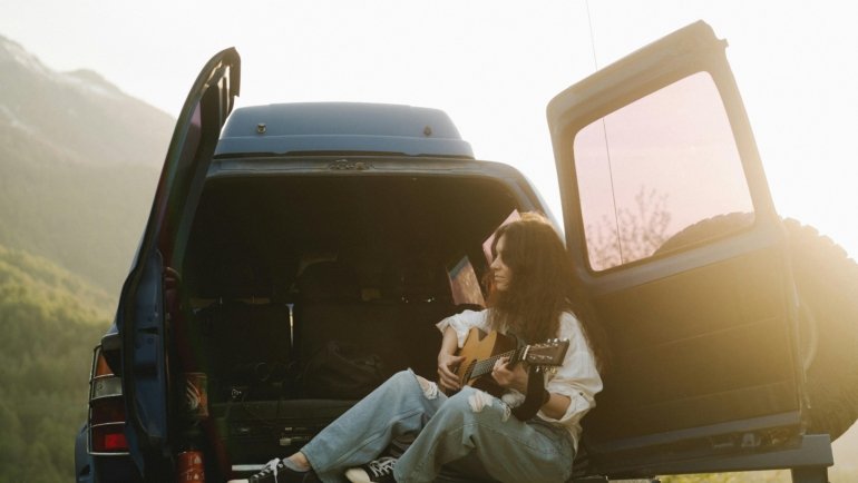 Musician playing a compact, portable travel guitar outdoors in a scenic landscape, representing the freedom of music for travel and adventure.