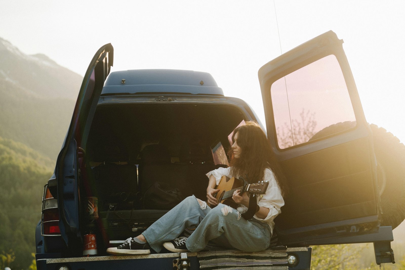 Musician playing a compact, portable travel guitar outdoors in a scenic landscape, representing the freedom of music for travel and adventure.