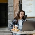 A person's hand comfortably using a compact wireless travel mouse with a laptop in a modern cafe, showcasing enhanced productivity and ergonomic comfort for remote work and digital nomads.