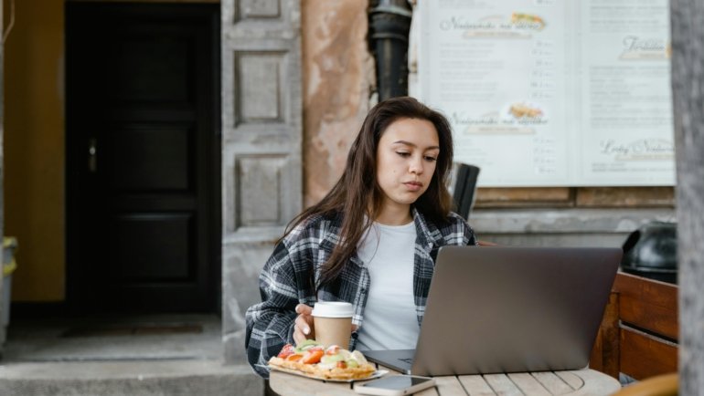 A person's hand comfortably using a compact wireless travel mouse with a laptop in a modern cafe, showcasing enhanced productivity and ergonomic comfort for remote work and digital nomads.