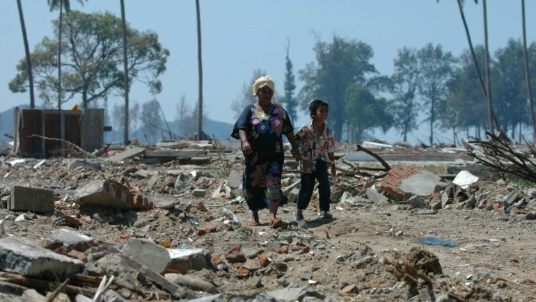 An aerial wide-angle shot of a massive tsunami's aftermath, showing debris and water inundation stretching far inland from the original coastline, highlighting the extensive reach of these powerful waves.