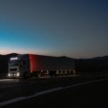 A professional semi-truck driving on Interstate 5 towards a modern truck stop, representing the impact of the TA Travel Center closure in Corning, CA, on long-haul drivers needing fuel, food, and rest alternatives.