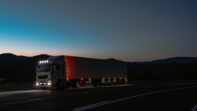 A professional semi-truck driving on Interstate 5 towards a modern truck stop, representing the impact of the TA Travel Center closure in Corning, CA, on long-haul drivers needing fuel, food, and rest alternatives.