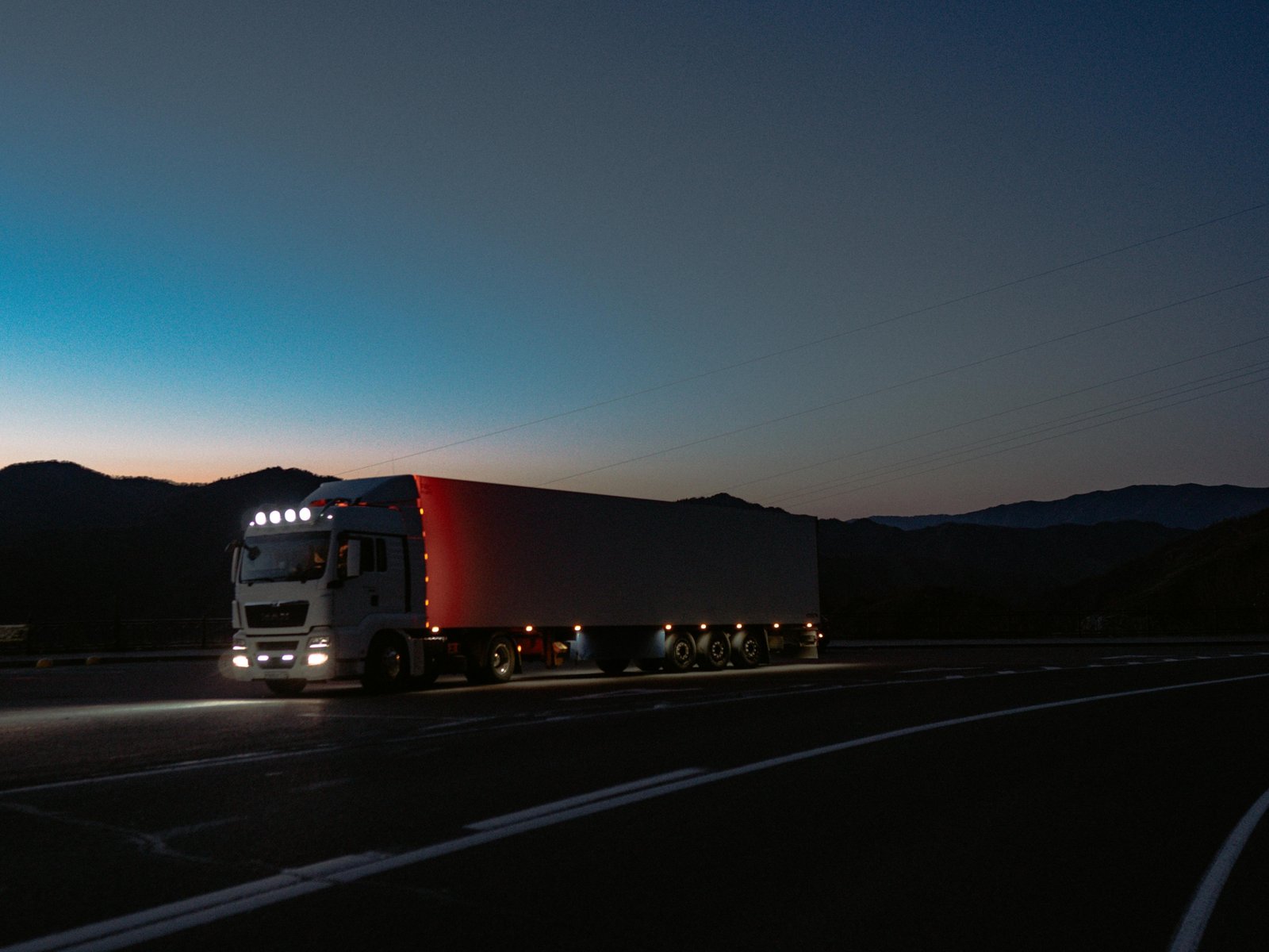 A professional semi-truck driving on Interstate 5 towards a modern truck stop, representing the impact of the TA Travel Center closure in Corning, CA, on long-haul drivers needing fuel, food, and rest alternatives.