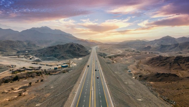 Modern Fort Independence Travel Plaza on Highway 395 in California's Eastern Sierra, featuring gas pumps, EV charging, and a variety of vehicles with mountains in the background, a vital stop for road trips.