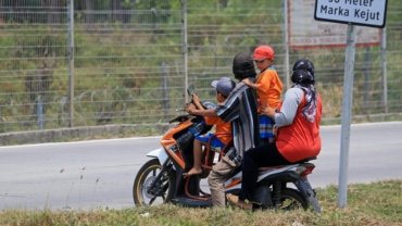 Child passenger safely riding a motorcycle with an adult, both wearing a reflective ride safe travel vest for secure family adventure.