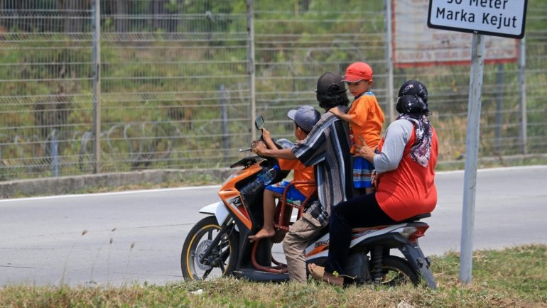 Child passenger safely riding a motorcycle with an adult, both wearing a reflective ride safe travel vest for secure family adventure.