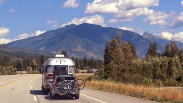 Inexpensive travel trailer parked in a scenic natural setting with a couple enjoying the view, symbolizing affordable road trip freedom and budget camping adventures.