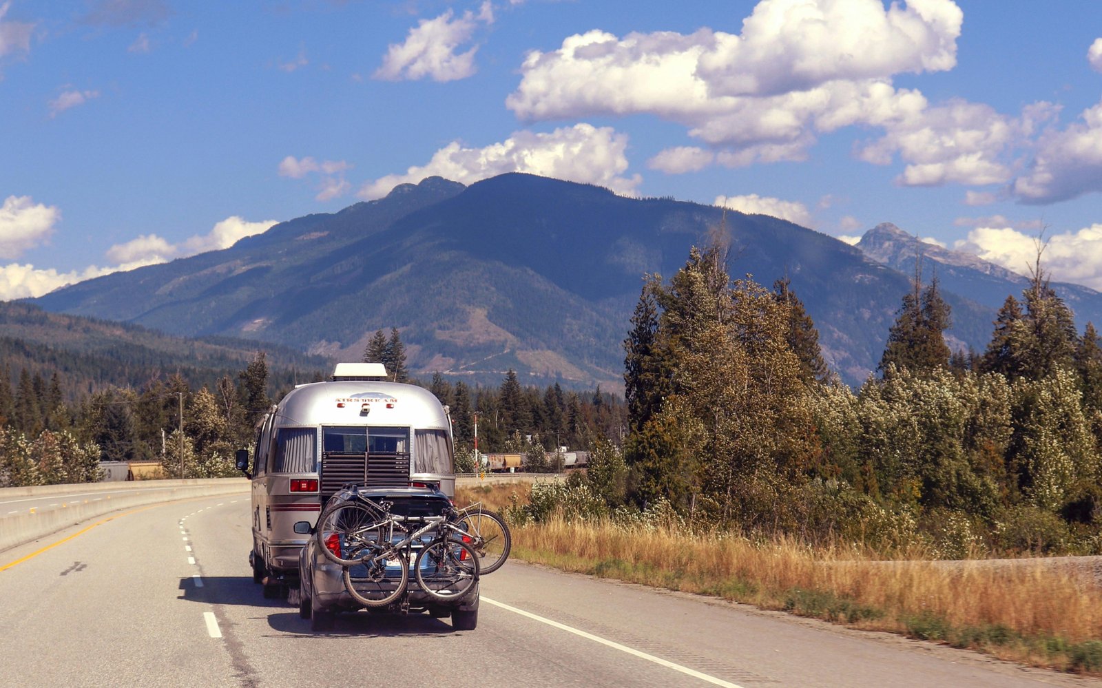 Inexpensive travel trailer parked in a scenic natural setting with a couple enjoying the view, symbolizing affordable road trip freedom and budget camping adventures.