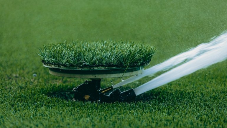 An Orbit traveling sprinkler actively watering a beautiful green lawn, demonstrating automatic, self-propelled garden irrigation for efficient and time-saving lawn care.