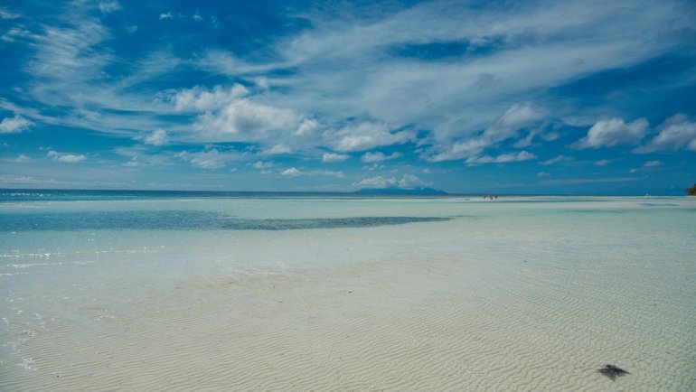 Person relaxing on a beautiful tropical beach with white sand and clear turquoise water under a sunny sky, ideal for a warm November travel escape or sunny getaway.