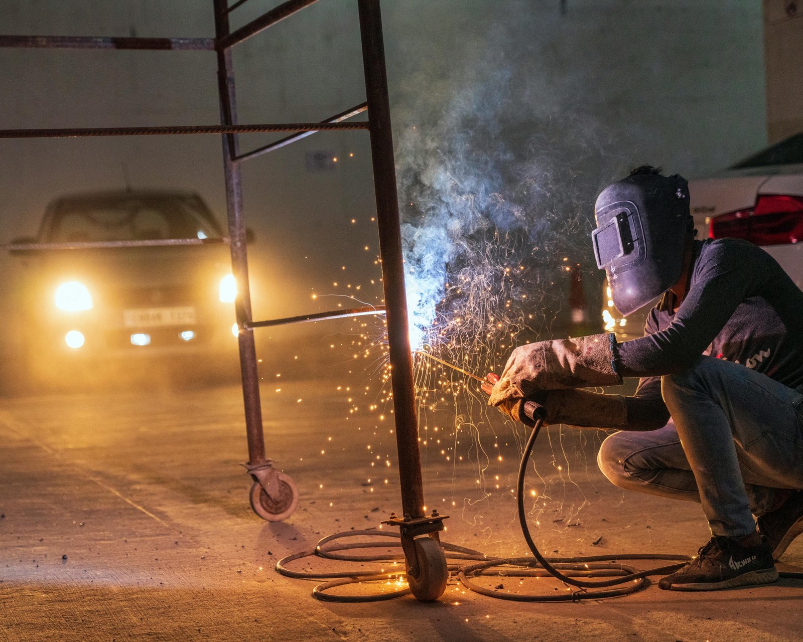 Professional traveling welder in full gear creating bright sparks while working on a large industrial pipeline or construction site, representing skilled journeyman welding.
